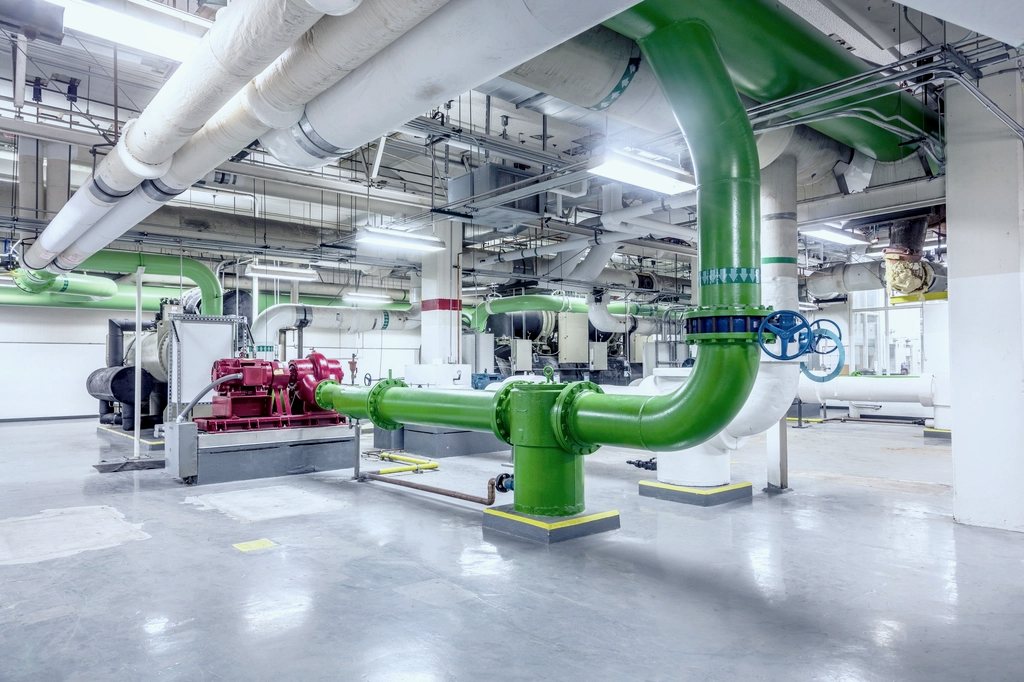 A large mechanical plant room with colour-coded headers, pumps and a clear floor.